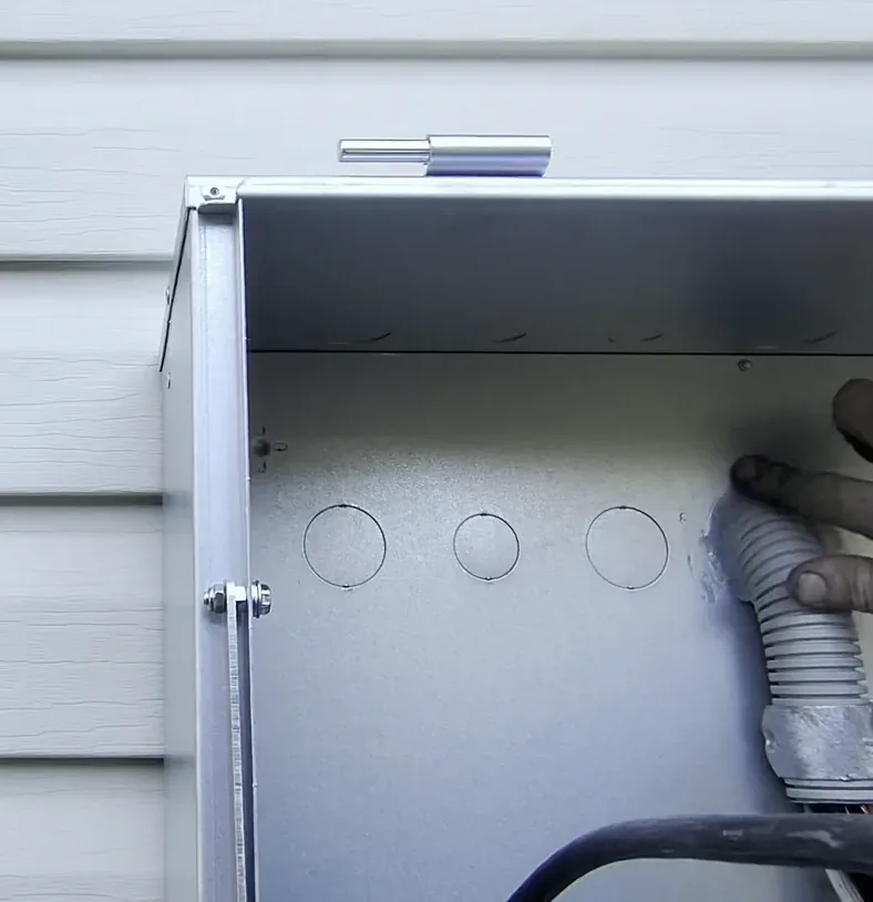 Open service enclosure on a weatherboard wall with the incoming conduit entering the base